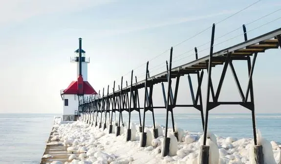 A lighthouse at the end of a pier covered in snow and ice